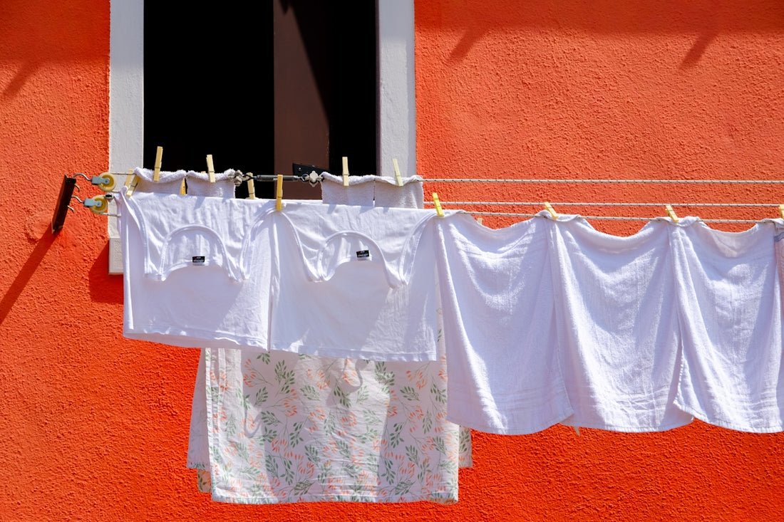 White laundry hangs on a clothesline against an orange wall.